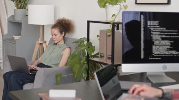 在总部工作的年轻白种人女程序员和难以辨认的男同事在Pan中等速度下一起在手提电脑上输入程序代码和聊天 — 图库视频影像