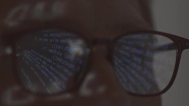 Extreme closeup of man in eyeglasses with program code reflected in them from projector
