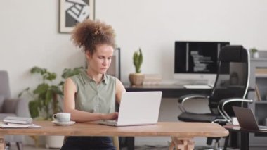 Medium stab shot of serious Caucasian female programmer working on laptop at home office with program codes running on black screen of pc computer in background