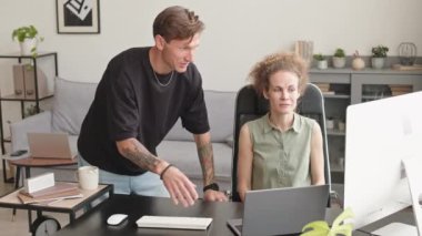 Medium slowmo of creative couple of graphic designers sharing ideas on new project looking at laptop screen, working together in contemporary workspace