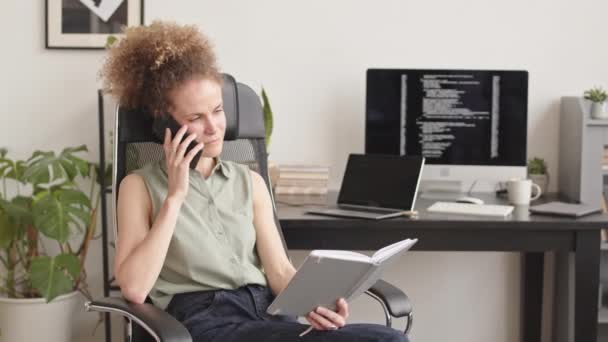 Medium Slowmo Του Γυναικείου Προγραμματιστή Κοιτάζοντας Σημειωματάριο Και Έχοντας Τηλεφωνική — Αρχείο Βίντεο
