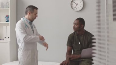 Kolunda kol askısı olan, beyaz laboratuvar önlüklü doktorla konuşan Afrikalı Amerikalı askerlerin orta derece yavaşlığı.