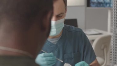 Afrika kökenli Amerikan subayından ağız örneği alan beyaz maskeli erkek doktor belini yavaşça yukarı kaldırın ve onu omikron testi yapın.