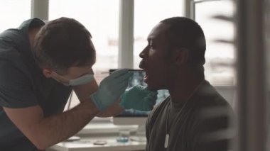 Waist up slowmo of African American army officer in khaki being tested for covid or omicron by male nurse taking mouth swab from him