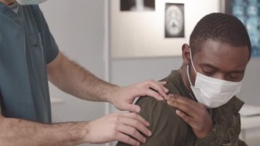 Orta ölçekli Afrika kökenli Amerikan askerinin omuz çıkığı ordu doktoru tarafından inceleniyor.