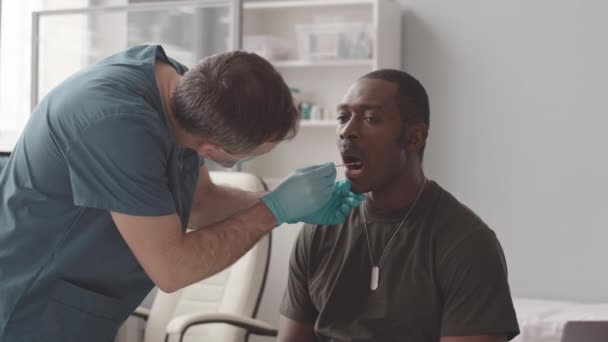 顔のマスクで白人男性看護師の中程度の遅いです口のスワブからアフリカ系アメリカ人兵士テスト彼のためのオミクロンまたはCovid — ストック動画