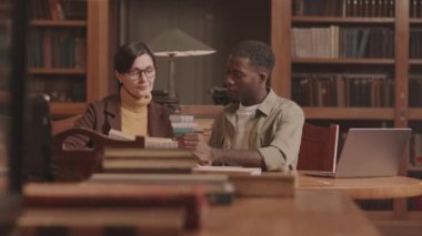 Orta yaşlı Afrikalı Amerikalı erkek üniversite öğrencisi ve kütüphanede okuyan beyaz kadın profesör. Masasında kitap ve dizüstü bilgisayarla oturuyorlar.
