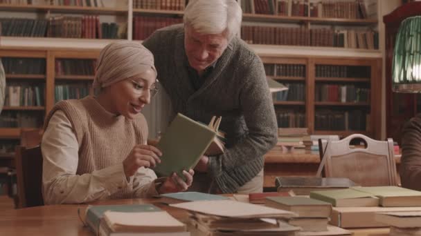 戴着眼镜 头戴头巾 头戴白色头巾的年轻穆斯林妇女慢吞吞地在图书馆讨论着书的情节 — 图库视频影像