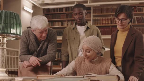 図書館で会話をする4人の若者と成人の多民族グループの中低速 — ストック動画