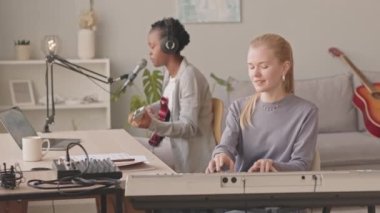 Amatör müzik stüdyosundaki Z jenerasyonunun orta yavaş kadın müzik ikilisi. Piyanist klavye çalarken, siyah bir kadın mikrofonla gitar çalıp şarkı söylüyor.