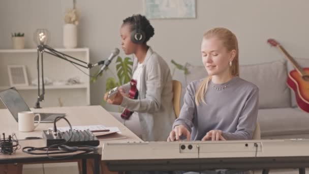 ホーム レコード ミュージック スタジオでのゲン Z多民族女性音楽デュオ レコーディング ソングの中遅い 黒人女性はエレキギターを演奏し ピアノはキーボードを演奏しながらマイクで歌う — ストック動画