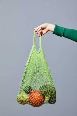 Gri arka plan, bilinçli tüketim vegan konseptine karşı sebzeli ekolojik alışveriş torbası.