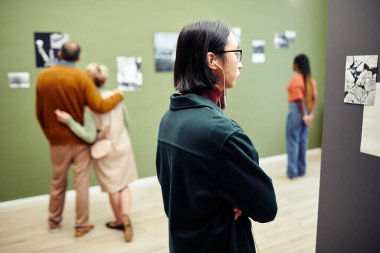 Modern fotoğraf sergisinde duvarlarda asılı çağdaş siyah beyaz fotoğraflara bakan etnik çeşitliliğe sahip insanlar