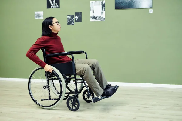 Portrait of modern young Asian man with disability in wheelchair visiting abstract photography exhibition in art gallery