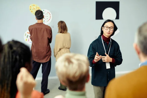 展覧会で発表された現代美術について語る観光客のグループの前に立つ若いアジアのギャラリスト — ストック写真