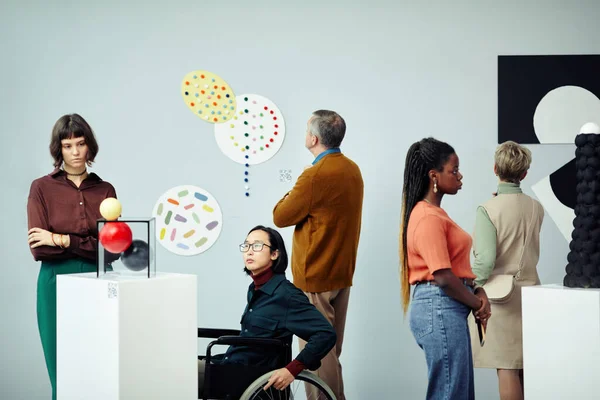 Group of diverse multi-ethnic people looking at various contemporary art objects at exhibition in modern museum