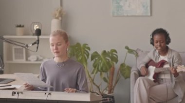 Ev müziği stüdyosunda yeni bir şarkı prova eden çok ırklı genç kadın müzik düetinin orta yavaşlığı. Bir kız klavye çalarken, diğeri kulaklıkla gitar çalıyor.