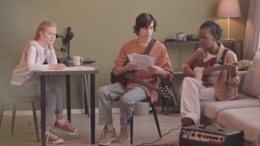 Slowmo of young various music band playing music enstruments and making new song together at home music studio