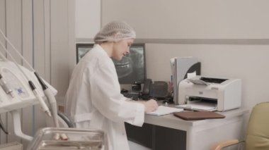 Kafkasyalı genç bir dişçinin orta yavaş portresi bilgisayarın önünde oturmuş hasta dişleriyle röntgen çektirip kameraya gülümsüyor ve işinden zevk alıyor.