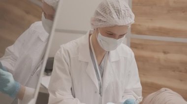 Beyaz laboratuvar önlüğü ve yüz maskesi takmış, elinde tıbbi aletlerle çağdaş klinikteki diş muayenesinde hastaların dişlerini inceleyen Kafkas kadın stomatologların yavaşlaması.