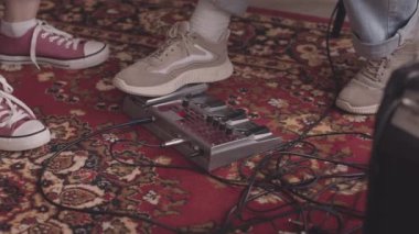 Spor ayakkabılı, tanınmayan gitaristin arka plandaki halının üzerinde elektro gitar pedalına basıp arkadaşlarıyla birlikte stüdyoda müzik çaldığı düşük bölüm.