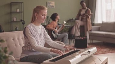 Klavye çalan Kafkasyalı genç bir kadının çok ırklı müzik grubuyla konser provası yaparken ev stüdyosunda bas ve elektro gitar çalmasının orta yavaşlığı.
