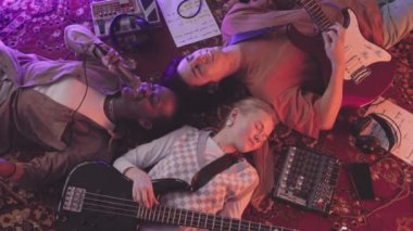 Neon ışıklandırmada klasik halıda uzanan ve müzik enstrümanları çalıp şarkı söyleyen çeşitli gen z müzik bandının yavaşlığından.