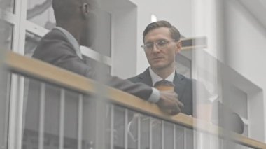 Düşük açı, iki kendine güvenen iş adamının ağırdan alması modern iş merkezinde cam korkuluklarda dikilip sohbet etmesidir.