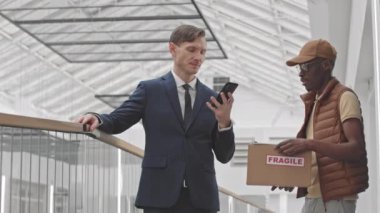 Afrika kökenli Amerikalı kuryenin beyaz başarılı iş adamına karton kutuda paket teslim etmesinin orta yavaşlığı. Girişimci belgeleri imzaladı ve nFC ile paket için ödeme yaptı