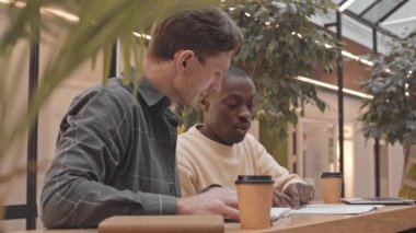 Aylık raporları analiz ederek ve iş hakkında konuşarak, rahat bir kafede rahat bir masada oturan iki girişimcinin belini yavaş yavaş kaldırın.