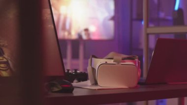 Bilgisayar monitöründe fps oyunu olan oyun salonunun masasında beyaz vr kulaklık ve denetçiyi yavaşlatan kimse yok.