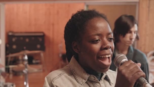 与情绪激动的年轻黑人妇女在录音室里用麦克风唱歌 而摇滚乐队则在录音室里背景音乐的中等特写 — 图库视频影像