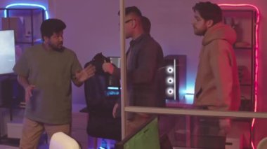 Oyun salonundaki neon ışıkla karanlık dumanlı odaya girerken konuşan çeşitli oyunculardan oluşan orta yavaş bir grup bilgisayar oyunlarında oynamaya hazırlanıyor.