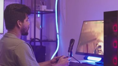 Oyun salonunda neon ışıklandırmayla oturan denetçiyle bilgisayarda fps oyunu oynayan iki yüzlü sakallı genç adam belini kaldır.