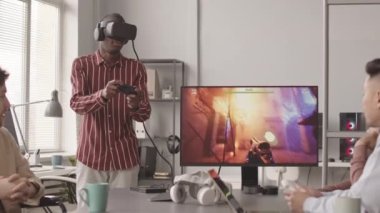 Ekibiyle birlikte geliştirdiği fps oyunu sırasında kontrol cihazını kullanarak VR kulaklıklı Afrikalı Amerikalı programcının orta yavaş çalışması.