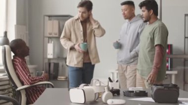 Ön planda iki VR kulaklığın orta yavaşlığı ve kahve molası sırasında konuşan, modern ofiste birlikte çalışan çok ırklı video oyunları geliştiricileri.