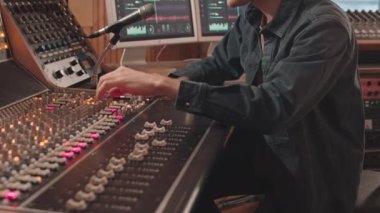 Genç beyaz adamın belini kaldır mikrofon kontrolüne konuşan ve profesyonel stüdyoda müzik kaydederken karıştırma konsolunu ayarlayan.