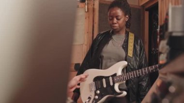 Deri ceketli, elektro gitarist ve prodüktörüyle konuşurken profesyonel müzik stüdyosunda yeni parça kaydeden Afrikalı Amerikalı genç bir kadın gitarist.