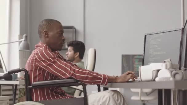 在与同事合作开发软件或游戏的过程中 轮椅打字程序代码中残疾的年轻非裔美国程序员的侧视中等速度 — 图库视频影像