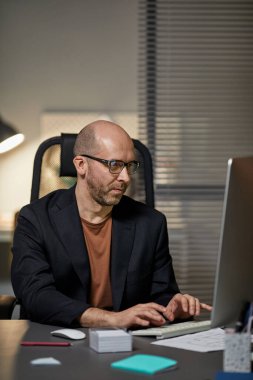 Gece geç saatlere kadar çalışırken bilgisayar kullanan kel iş adamının dikey portresi