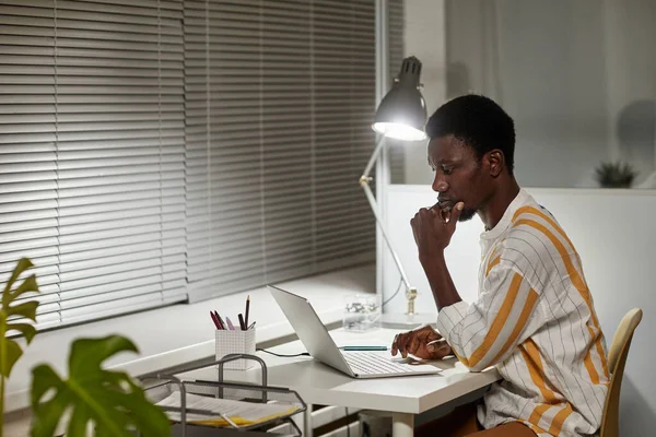 Minimal side view portrait of young African American man studying or working late at night, copy space