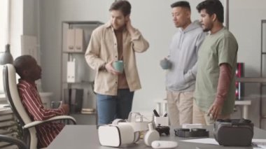 Ön planda iki VR kulaklığın orta yavaşlığı ve kahve molası sırasında konuşan, modern ofiste birlikte çalışan çok ırklı video oyunları geliştiricileri.