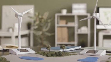 Hiç kimse yeşil duvarlı alternatif enerji mühendisi ofisinde arka planda güneş paneli olan rüzgar türbinlerinin modellerini ve peyzaj kağıt planını yavaşlatamaz.