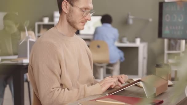 白种人年轻工程师在平板电脑上打字的速度为中等 同时与绿墙办公室的女同事一起从事替代能源项目 — 图库视频影像