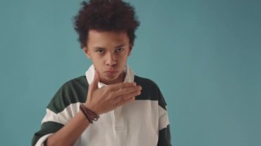 Melez 14 yaşındaki çocuğun orta yavaş portresi üzgün ve mutlu yüzler gösteriyor ve turkuaz arka planda duran sakızdan baloncuk yapıyor.