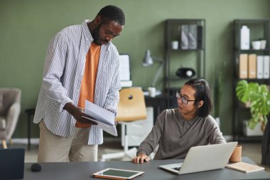 Asyalı meslektaşla konuşan Afrikalı Amerikalı bir adamın portresi ofisteki proje hakkında tavsiye istiyor