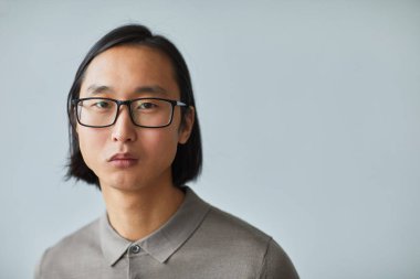 Asyalı genç işadamının gözlük taktığı ve stüdyoda açık mavi arkaplana bakarken kameraya baktığı minimal yakın plan portresi.