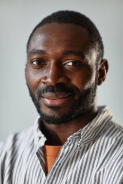 Stüdyoda yumuşak ışıkla aydınlatılan kameraya gülümseyen yetişkin siyahi adamın dikey yakın plan portresi