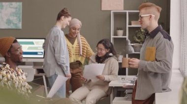 Tekerlekli sandalyedeki engelli, kahve molası sırasında Kafkasyalı meslektaşıyla konuşan siyahi bir adam. Arka planda iş belgelerini tartışan üç farklı genç kadın.