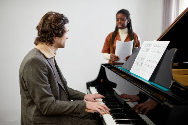 Genç öğretmen Afrikalı bir kadınla piyano çalıyor. Sınıfta tekrarladıkları sırada şarkının sözlerini öğreniyor.